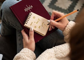 Woman writing in a notepad, planning her 2024 schedule. A cozy, indoor setting with a warm atmosphere.